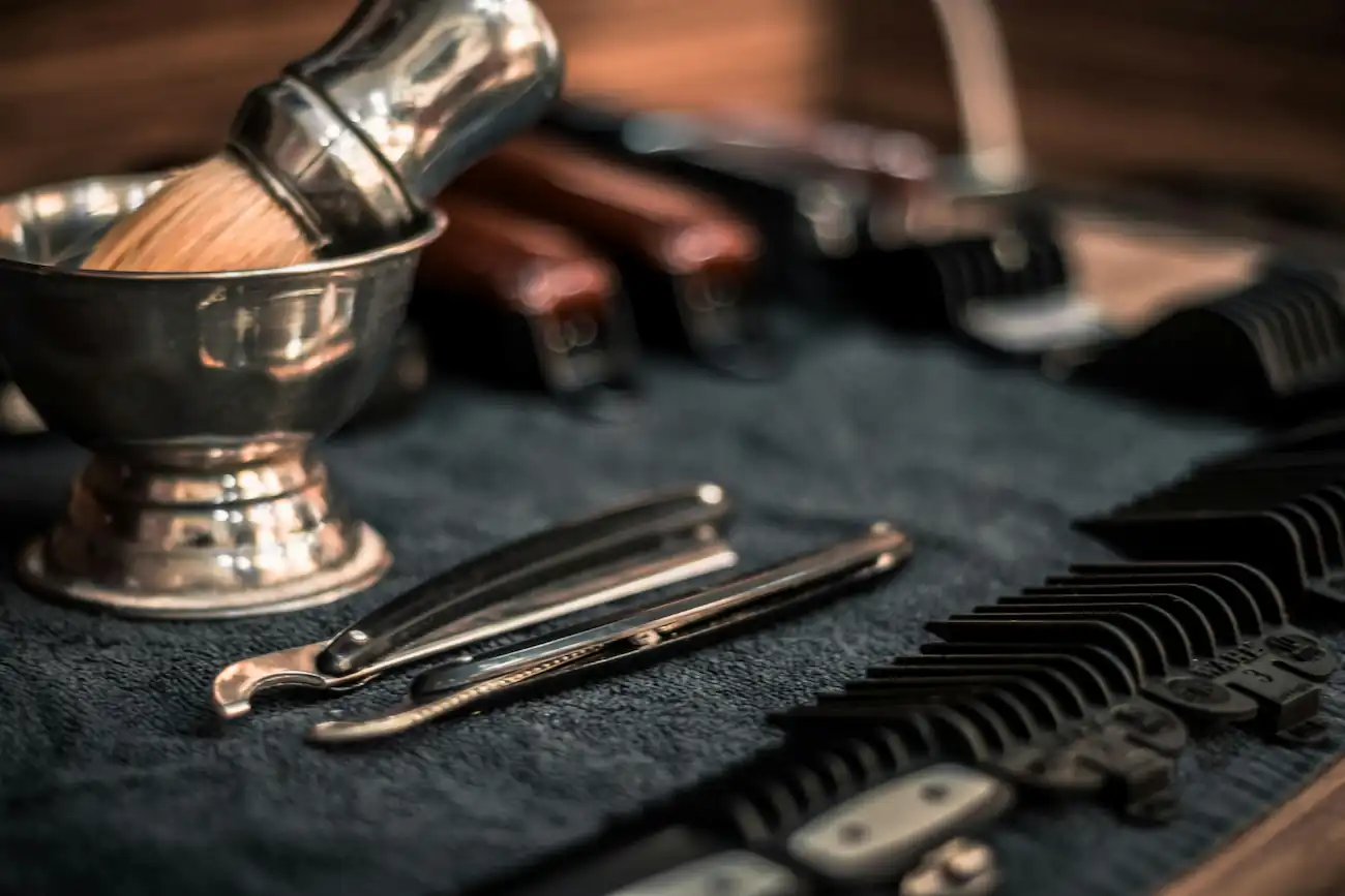 Straight razors, a shaving brush in a bowl and clipper guards on a towel
